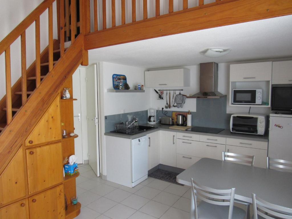une cuisine avec des placards blancs, une table et un escalier dans l'établissement Maisonnette avec Piscine, Terrasse et Jardin Privé - La Faute-sur-Mer - FR-1-194-282, à La Faute-sur-Mer