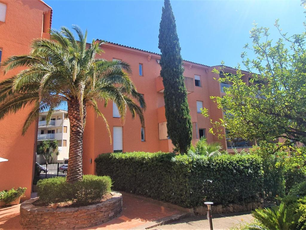 un bâtiment oranger avec des palmiers devant lui dans l'établissement Appartement 2 pièces avec clim, parking, proche commerces et plage - Sainte-Maxime, Golfe de St-Tropez - FR-1-780-76, à Sainte-Maxime