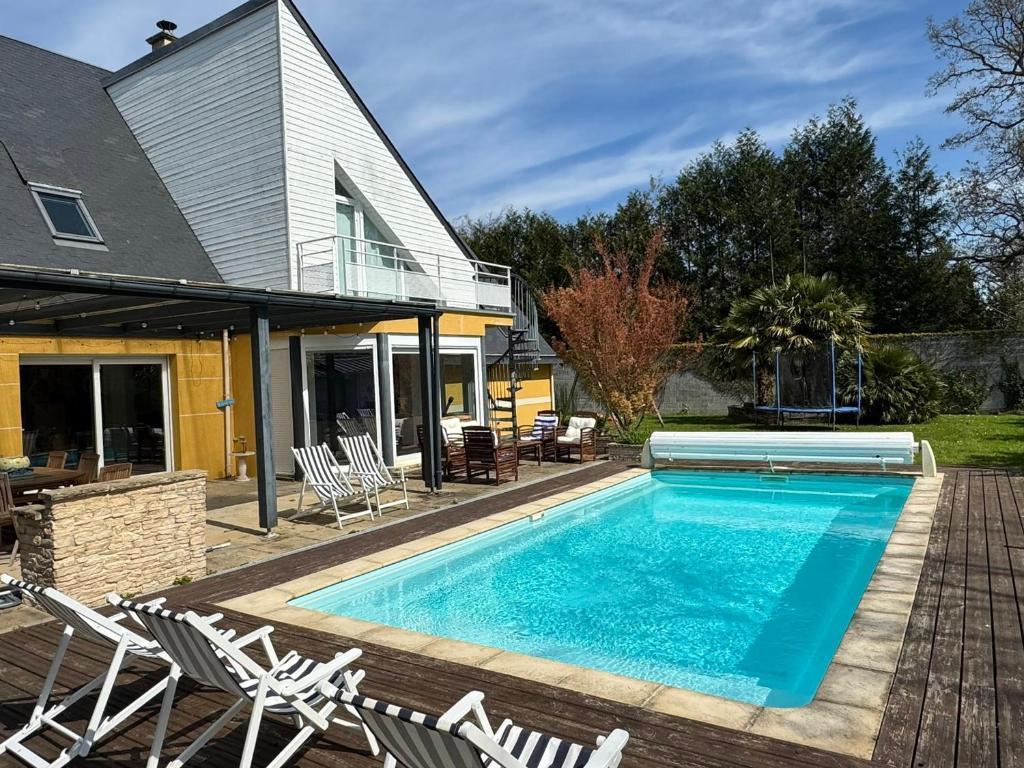 une piscine avec des chaises et une maison dans l'établissement Villa récente 4 chambres, piscine chauffée à Bavent - FR-1-487-380, à Bavent