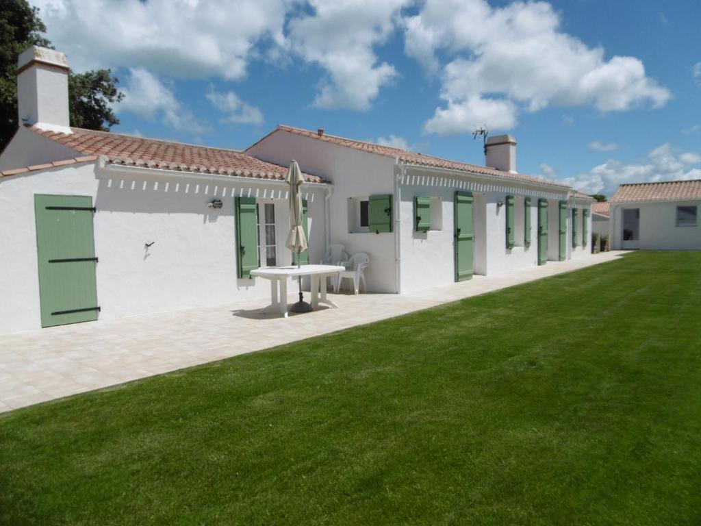 - un bâtiment blanc avec des portes vertes et une cour en gazon dans l'établissement Maison confortable à Noirmoutier pour 6 pers., proche plage - FR-1-823-104, à Noirmoutier-en-l'lle