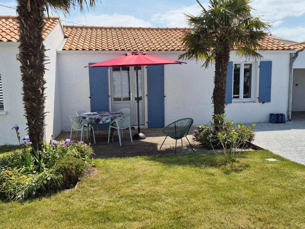 un patio avec une table, des chaises et un parasol rouge dans l'établissement Maison Noirmoutier entre Bourg et Plage, 4/6 pers, jardin, parking, TV, WiFi - FR-1-823-70, à Noirmoutier-en-l'lle