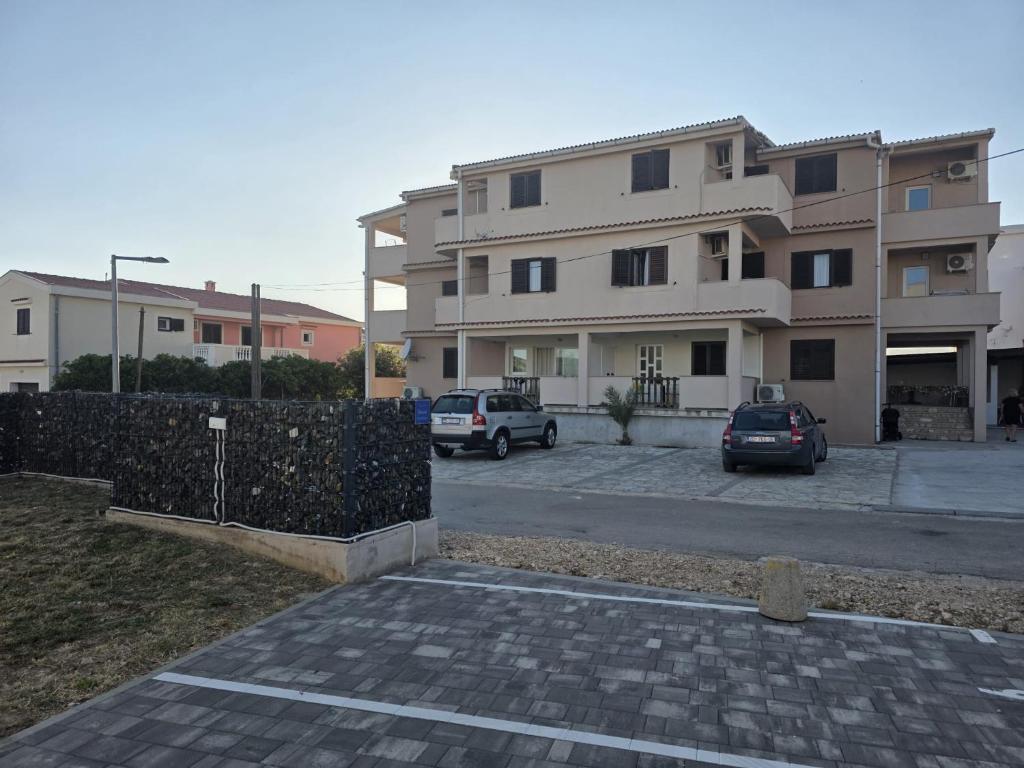 a building with cars parked in a parking lot at Budget Apartments Batkoski Pag in Pag