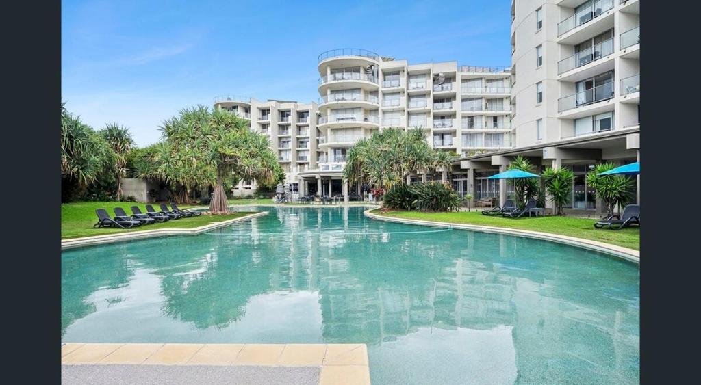 a swimming pool in front of a large apartment building at Rooftop Apartment - Heated Pool & Beach access in Marcoola