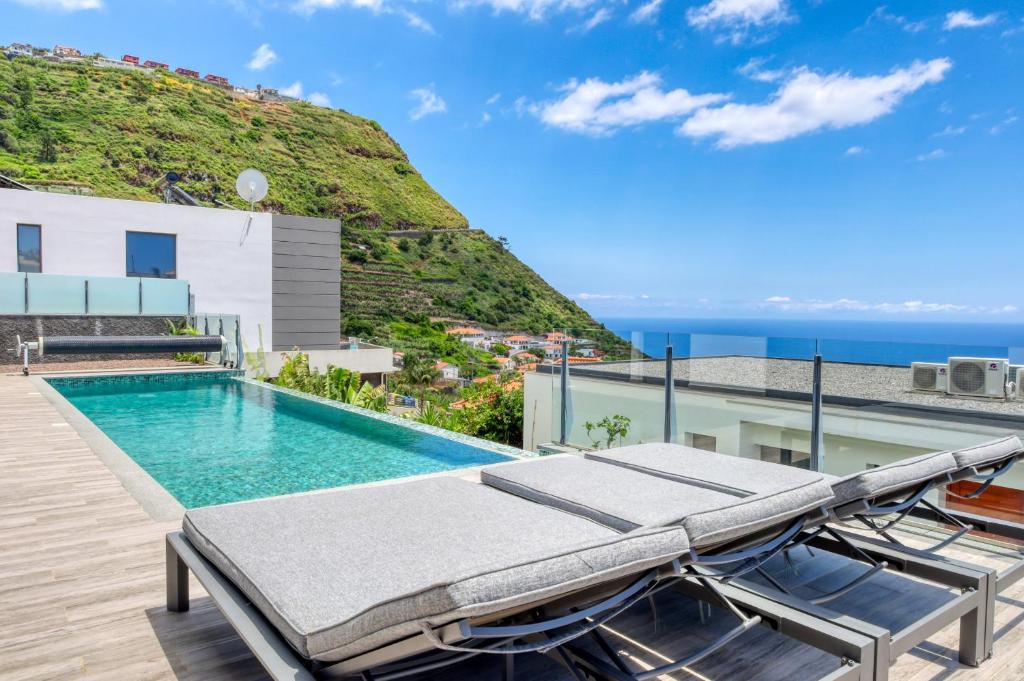einen Pool mit Liegestühlen und das Meer im Hintergrund in der Unterkunft Villa Arco-Iris, a Home in Madeira in Arco da Calheta