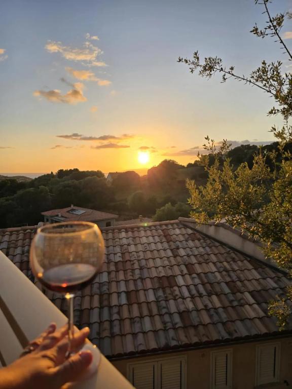 une personne tenant un verre de vin au coucher du soleil dans l'établissement Maison charmante à Propriano avec vue sur la montagne, à Propriano
