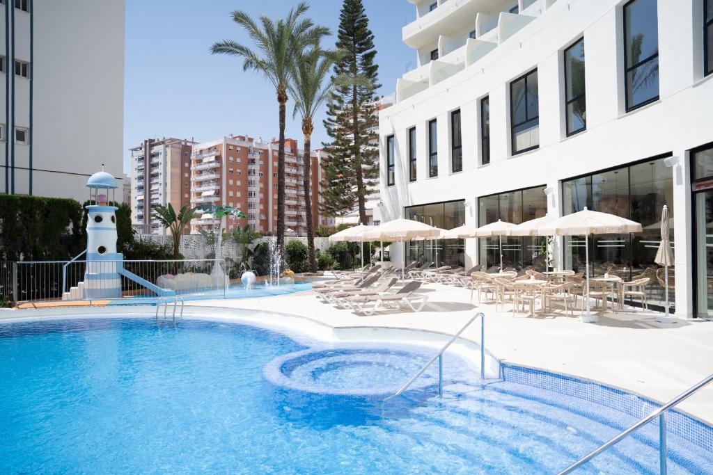 a swimming pool with chairs and umbrellas next to a building at Hotel RH Arena - Todo Incluido in Gandía