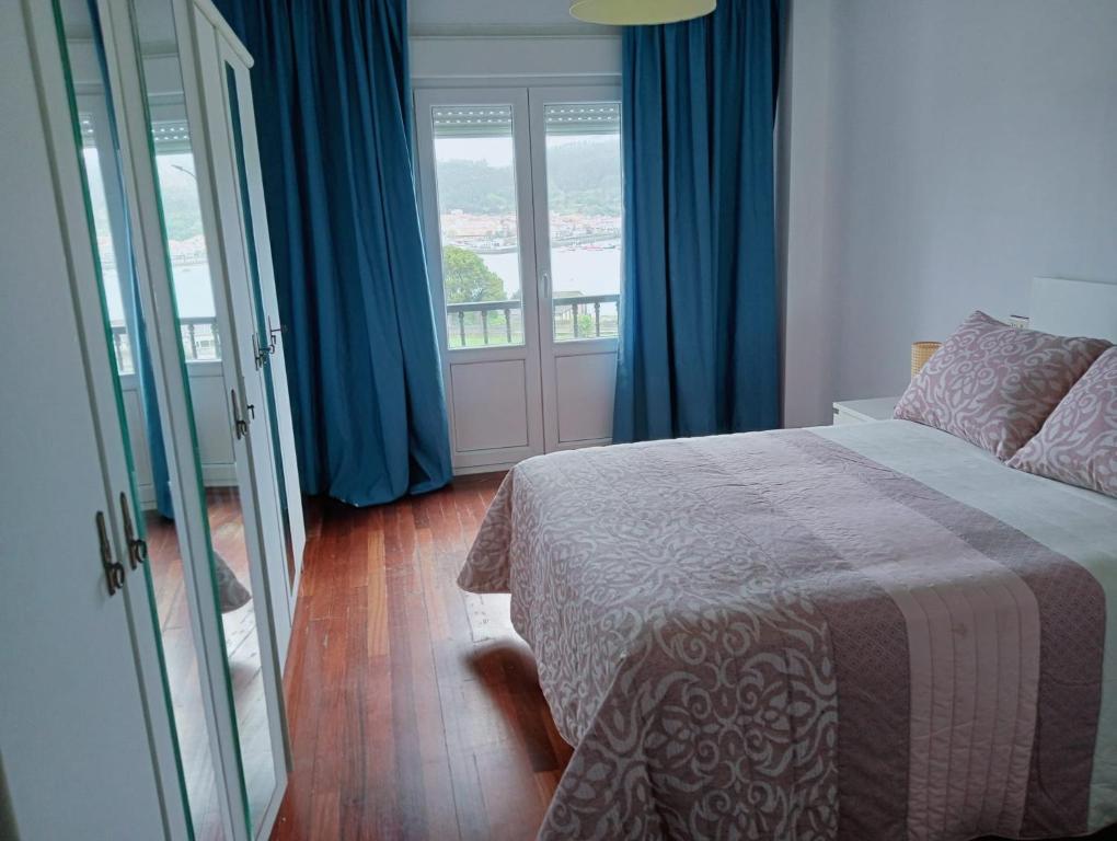 una camera da letto con letto, tende blu e finestra di Apartamento en Cee a Cee