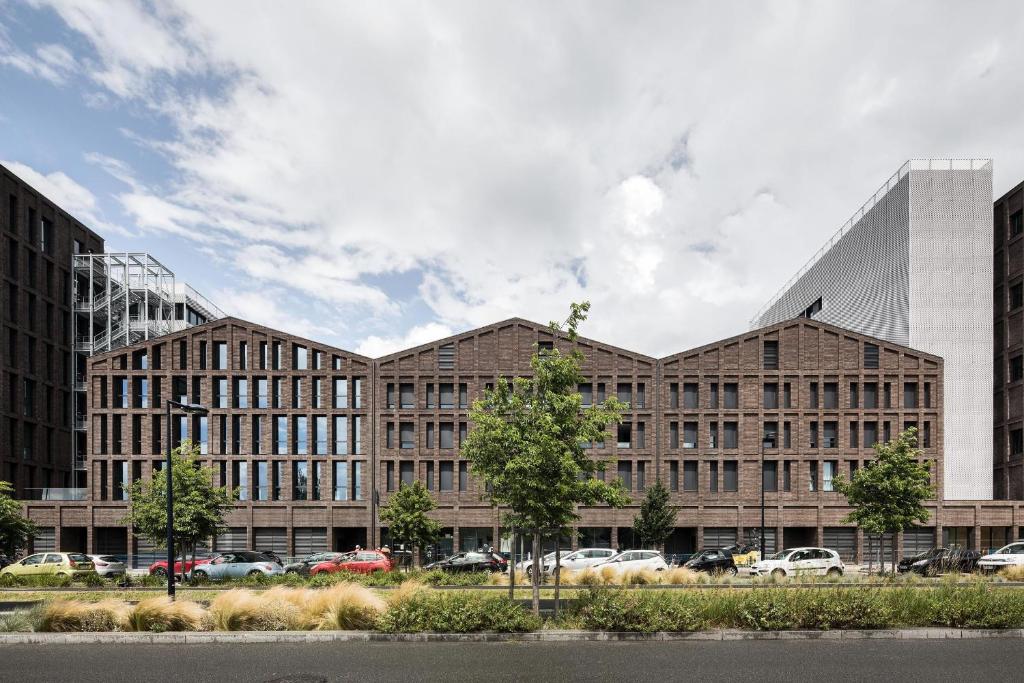 a large brick building with cars parked in a parking lot at Montempô Appart'Hôtel Bordeaux Centre - Bassins à flot in Bordeaux