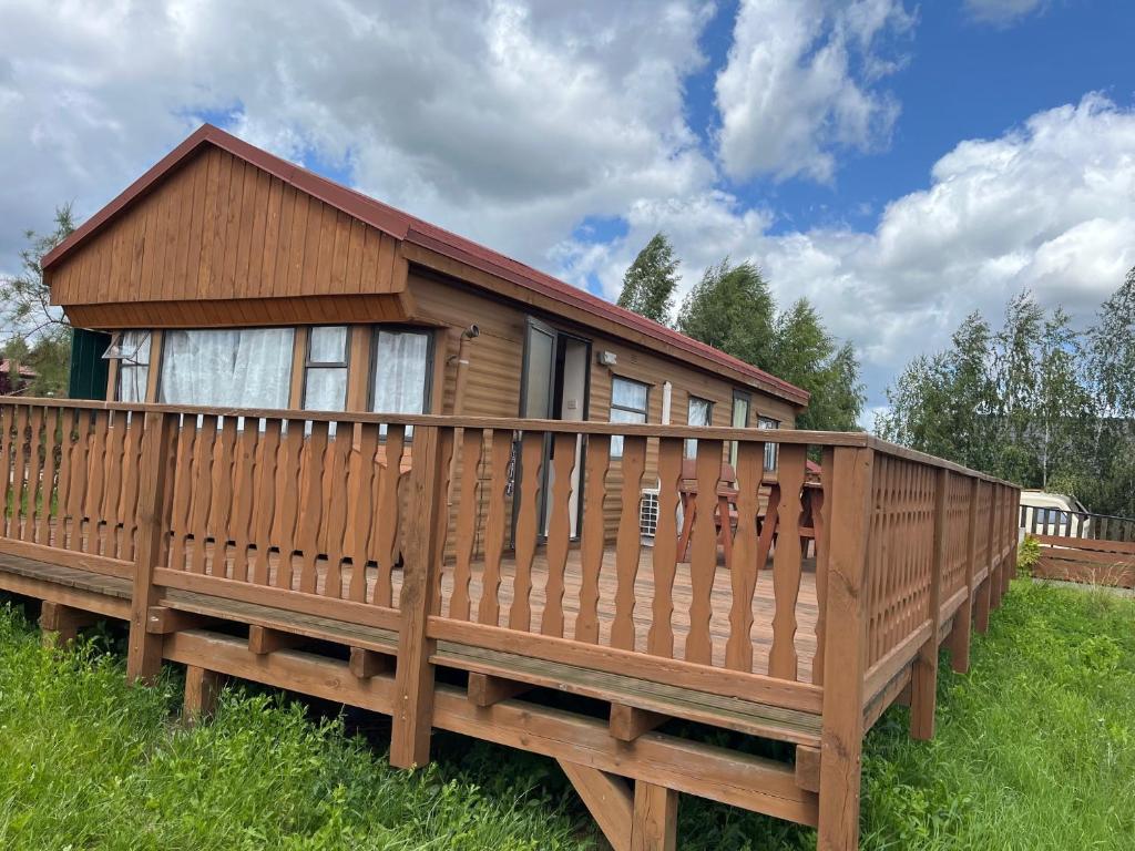 a wooden cabin with a large deck in the grass at Domek Czapla in Stare Sady