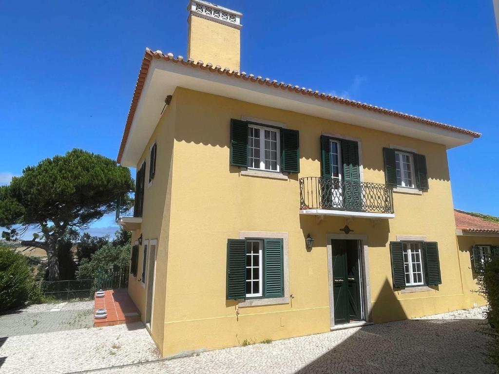 a yellow house with black shutters and a balcony at Elegant Villa Mello with Beautiful Outdoor Area in Lourinhã