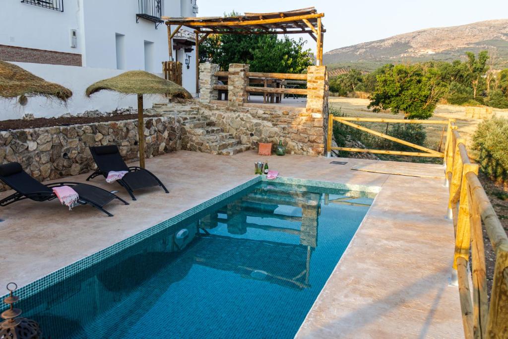 una piscina con dos sillas y una sombrilla en LA CASA DE LA HUERTA Stylish family cottage in Malaga countryside, en Málaga