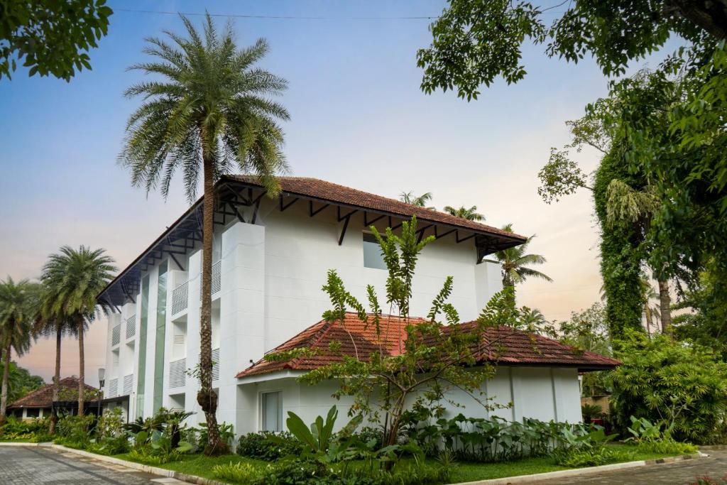 a white building with a red roof and palm trees at Hotel Riviera Garden in Cochin