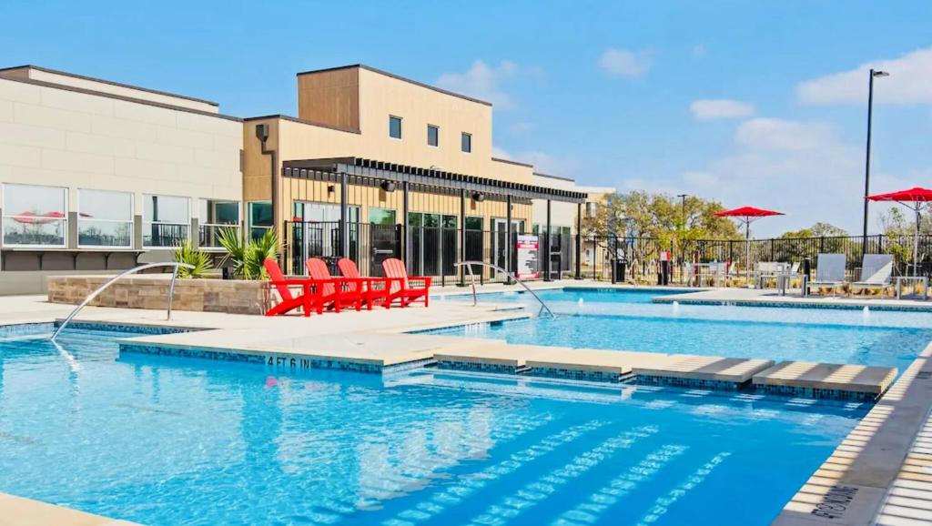 a swimming pool with red chairs in front of a building at Luxe 1B|Pool|Marble Falls Escape in Marble Falls
