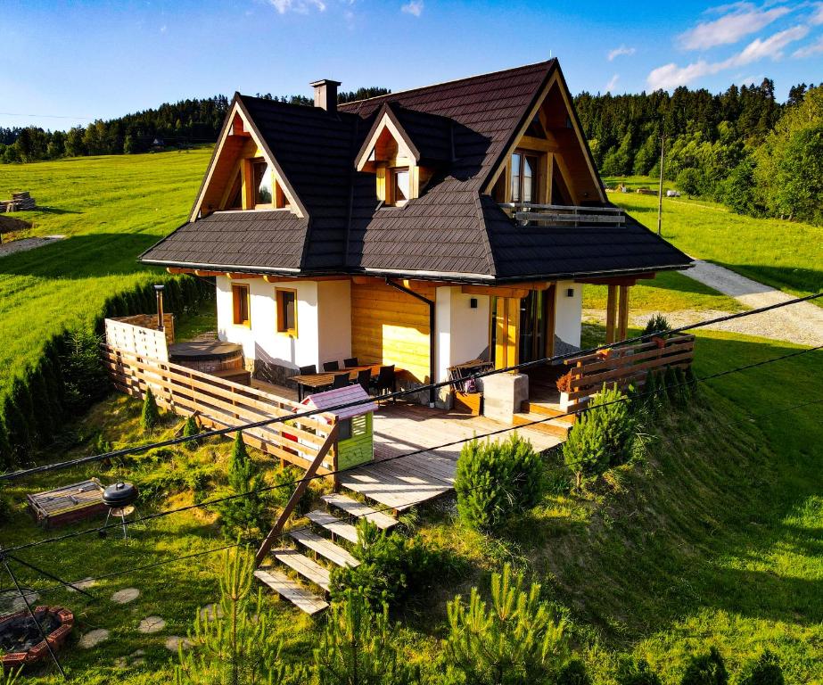 a house with a black roof on a green field at EM Gorce Resort komfortowe domki z sauną i jacuzzi in Waksmund