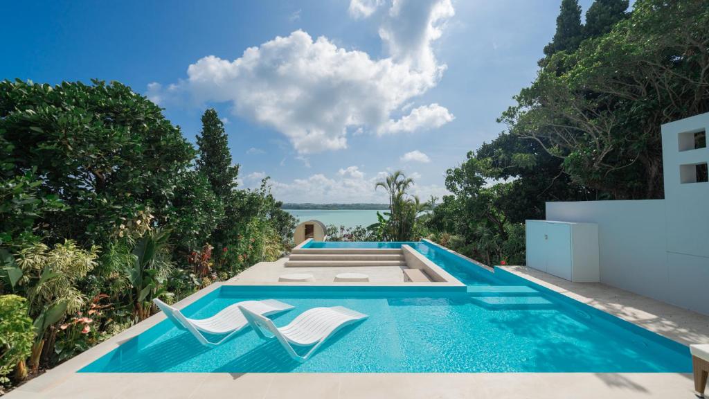 una piscina a sfioro con due sedie in cima a una casa di BAY COAST AGAIN miyakojima プライベートヴィラ ベイコーストアゲイン a Miyakojima