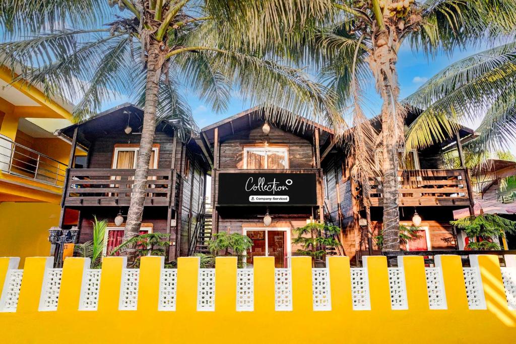 a yellow fence in front of a house with palm trees at Collection O Morjim Beach in Goa