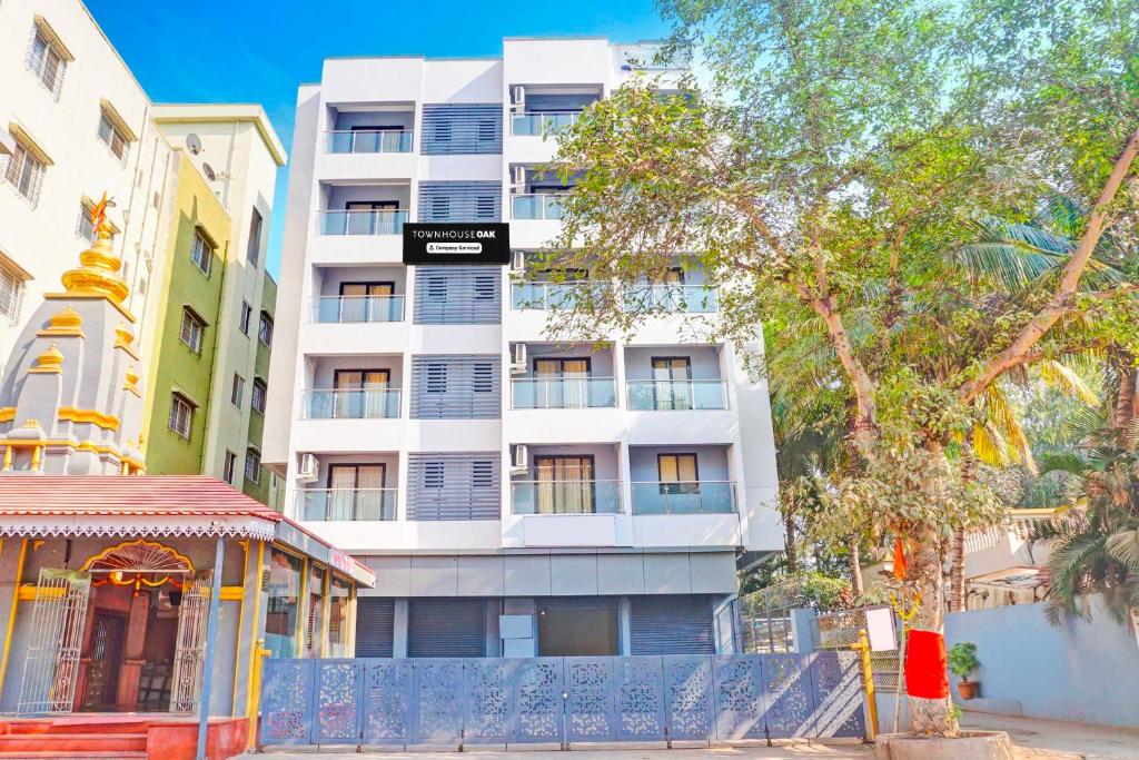 a tall white building with a tree in front of it at Townhouse Oak Pune Future Towers in Pune