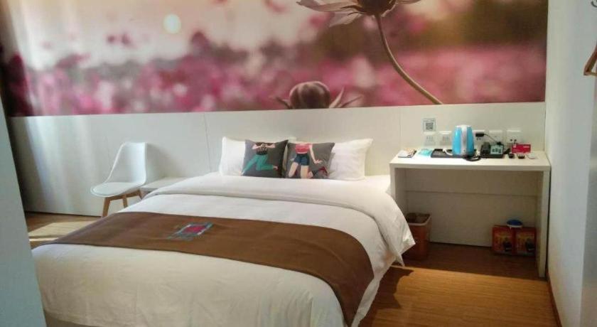a bedroom with a bed and a table with a painting at Pai Hotel Yanjiao Tianyang Plaza in Gaolou