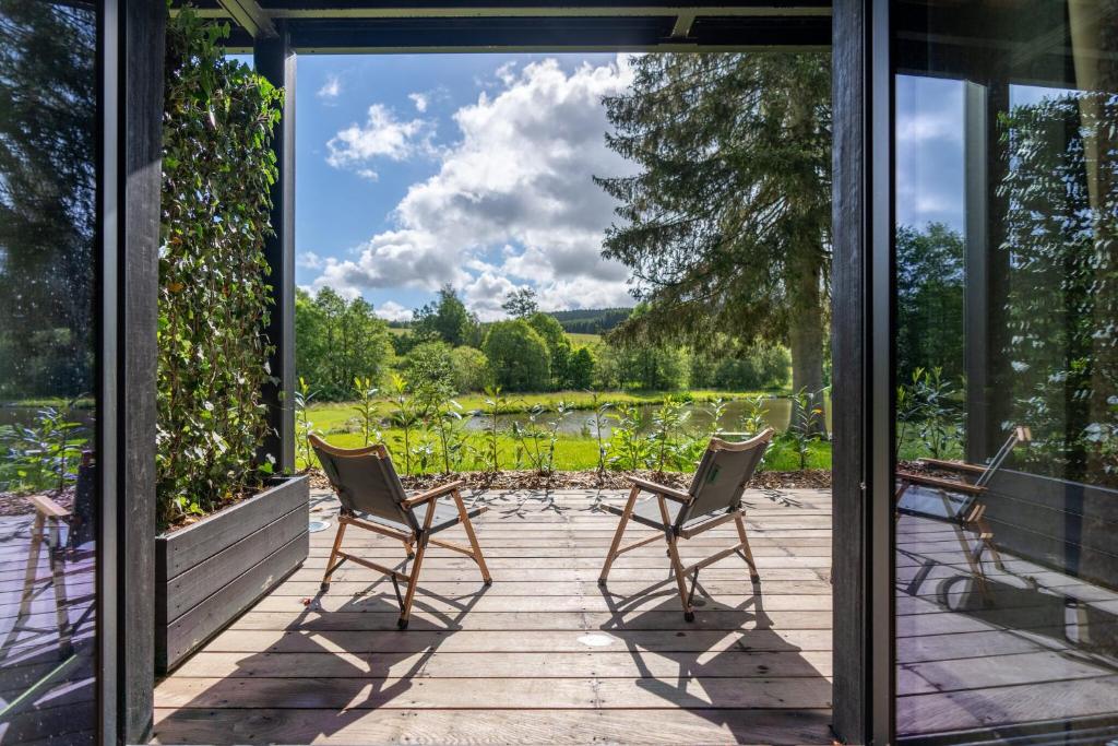 three chairs sitting on a porch looking out at a lake at Hillview Hotel Grandvoir in Neufchâteau