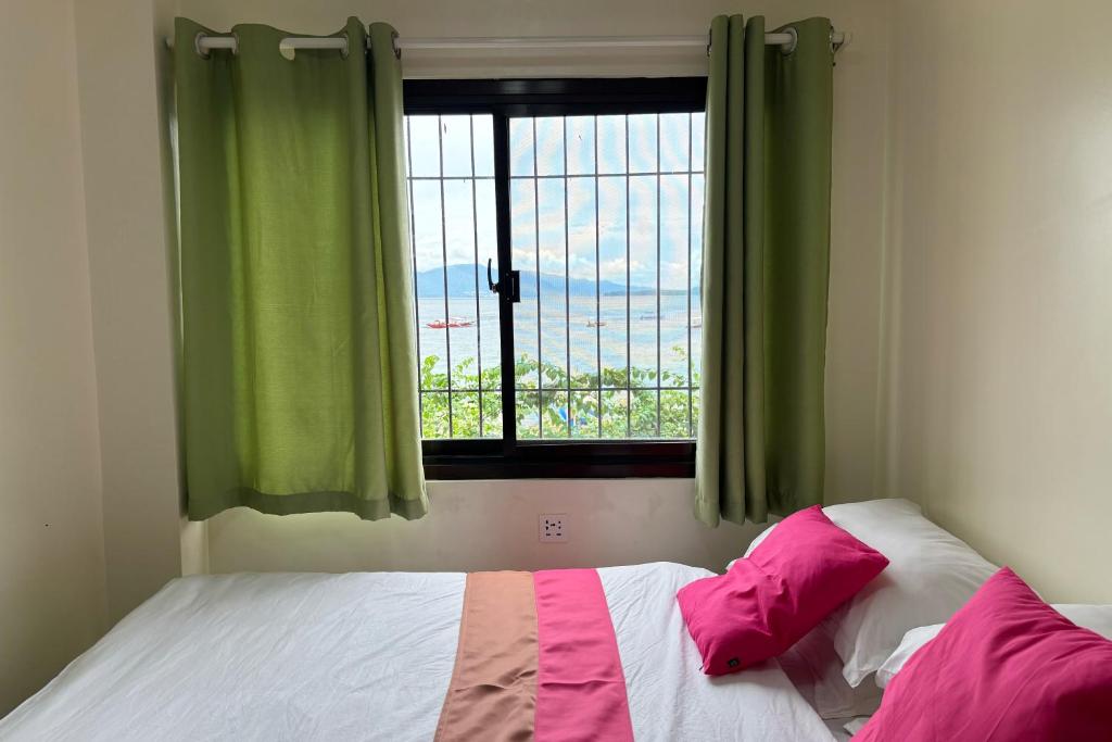 a bedroom with a bed and a window with green curtains at Pink Ocean Diving Resort Sabang Puerto Galera in Puerto Galera