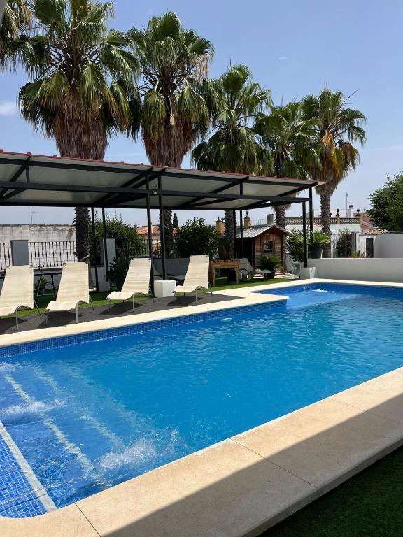 a swimming pool with chairs and a canopy and palm trees at Apartamento 1, Chalet Manzano a 15" de Sevilla, a 30" del Aeropuerto de Sevilla in Villanueva del Ariscal