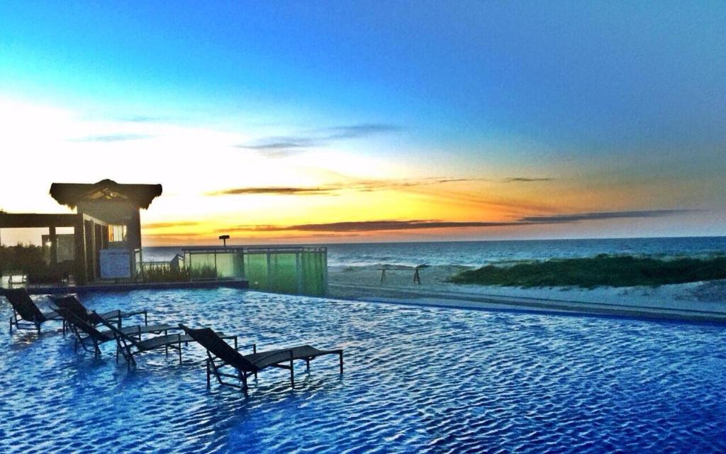 una piscina con sillas en la playa al atardecer en Beach Place Aquiraz Riviera, en Aquiraz