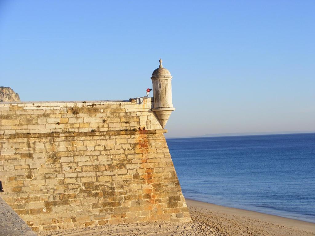 a lighthouse on a brick wall next to the ocean at Mar de Sesimbra in Sesimbra