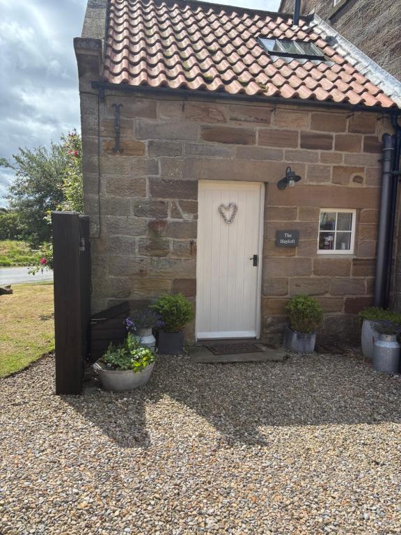 een stenen huis met een witte deur en potplanten bij The Hayloft Cottage in Whitby