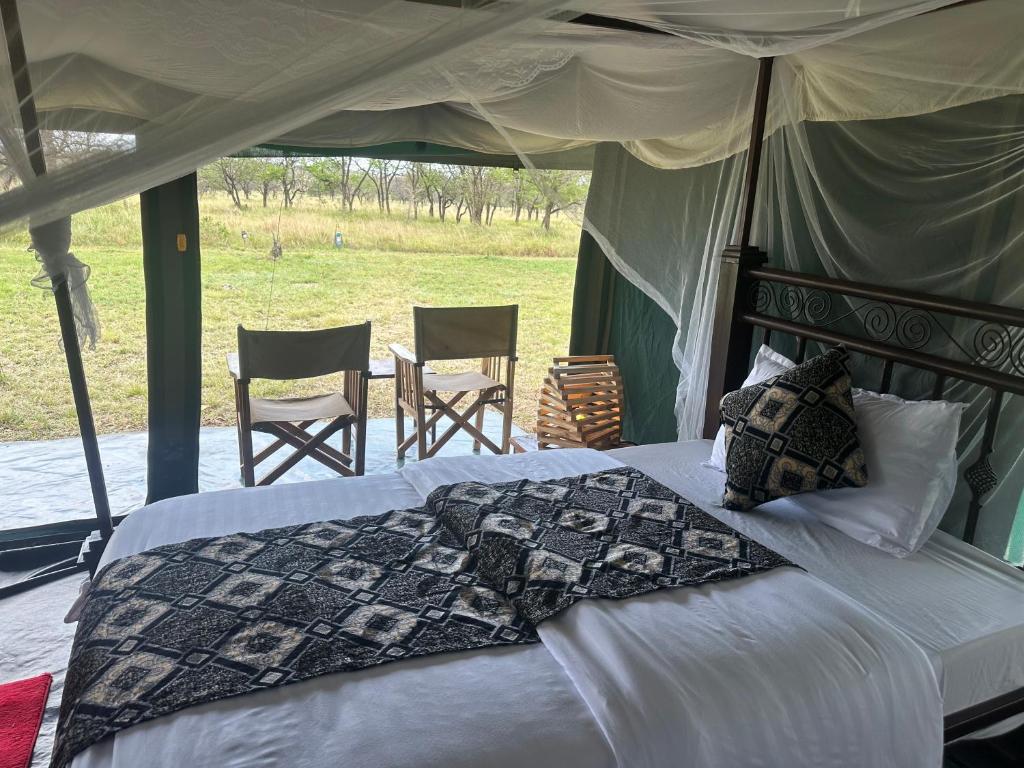 um quarto com uma cama em uma tenda com cadeiras em Zuhumath Tented Camps Serengeti em Parque Nacional Serengeti