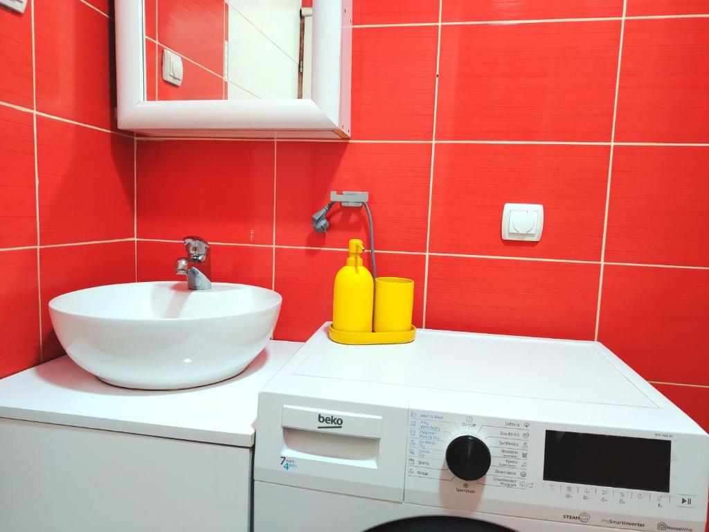 a red bathroom with a sink and a washing machine at City Center Sweet Apartment in Niš