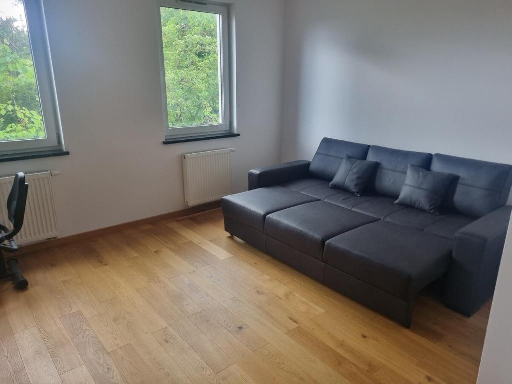 een woonkamer met een zwarte bank en 2 ramen bij Apt blisko morza in Kosakowo