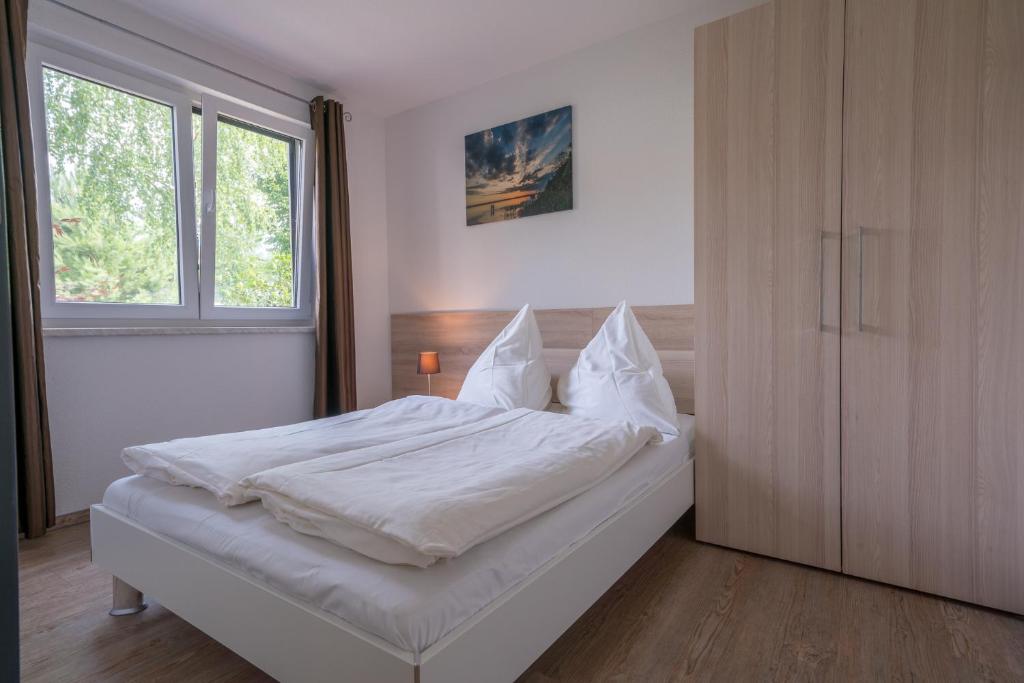 ein Schlafzimmer mit einem Bett mit weißen Laken und einem Fenster in der Unterkunft Ferienpark Rübezahl am Müggelsee, Haus 20 Mohn mit eigener Sauna, idealer Ort für Natur- und Erholungssuchende, für Radfahrer und Familien mit Kindern in Berlin