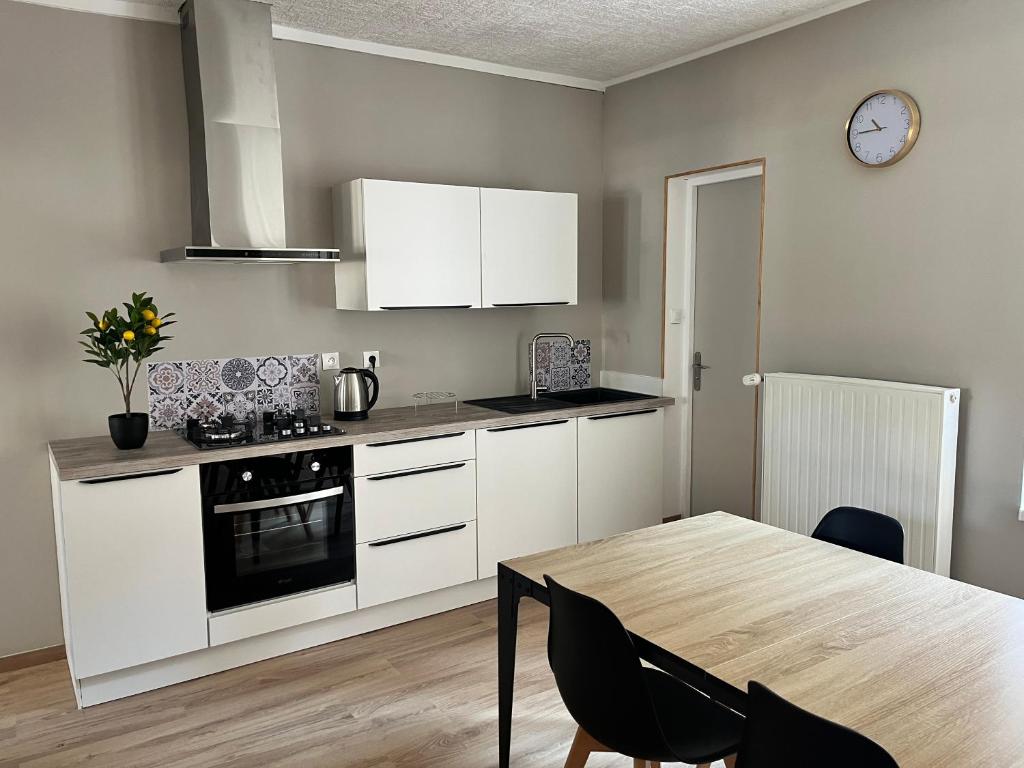 a kitchen with white cabinets and a table and a clock at Au cœur de la Meuse in Damvillers