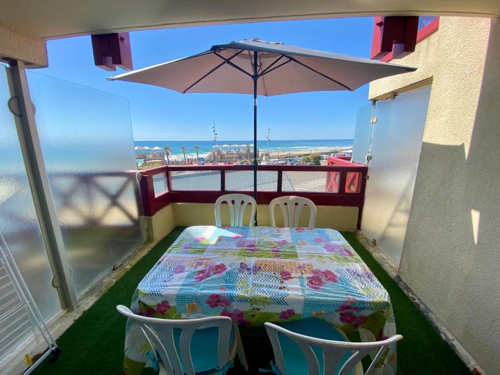 une table et des chaises sur un balcon avec un parasol dans l'établissement Appartement idéalement situé face à l'océan, à Lacanau