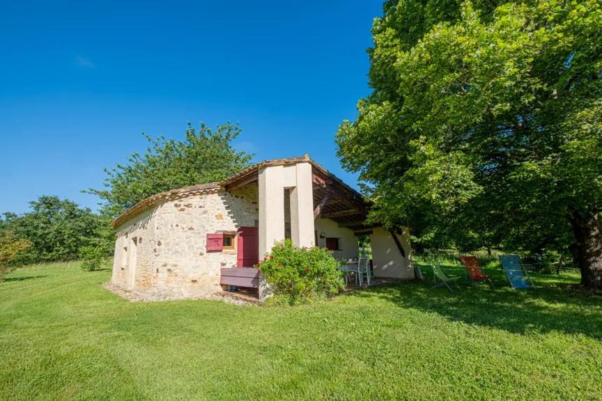 une vieille maison en pierre avec un arbre et un champ d'herbe dans l'établissement Gite le Cellier, à Gavaudun
