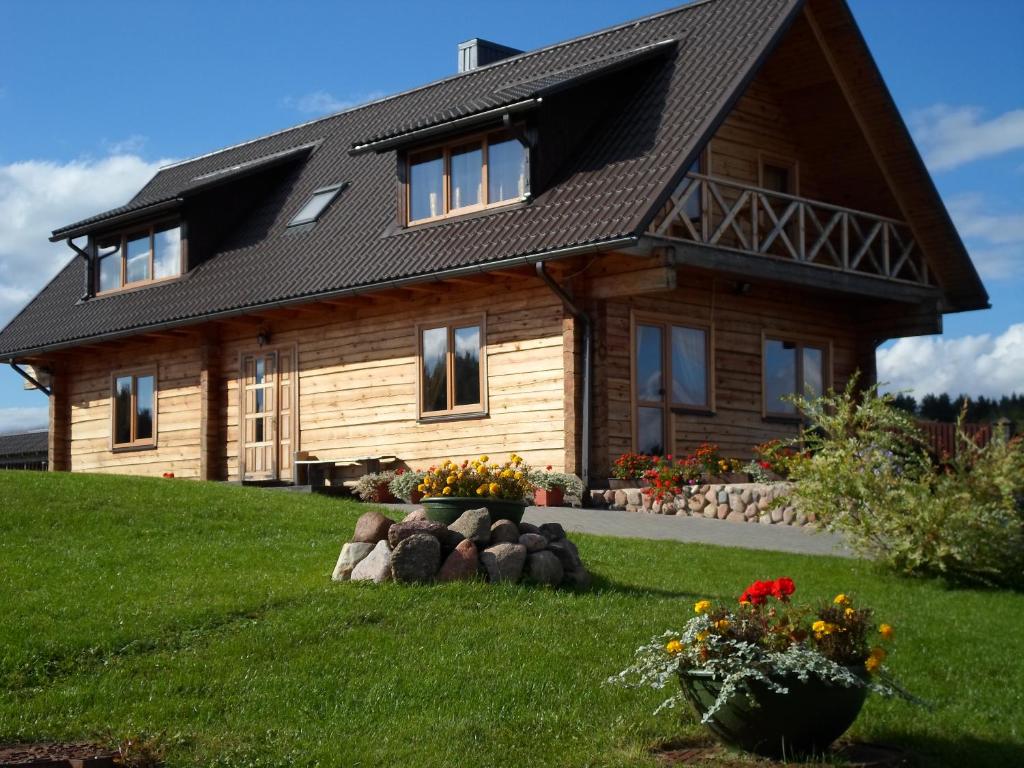 a wooden house on a hill with flowers in the yard at Romo sodyba in Trakai