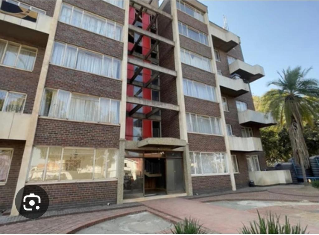a tall brick building with a palm tree in front of it at Bright & Airy 2BR in CBD Harare Modern with city view in Harare