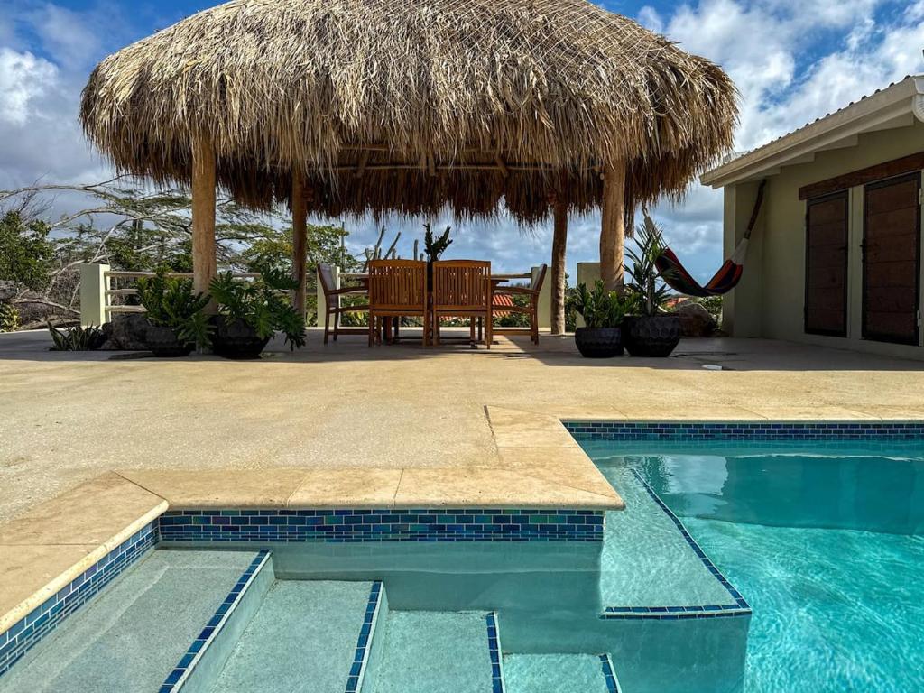 ノールトにあるPoolside Escape Menas Authentic Wellness Ecoのテーブルとわら傘付きのスイミングプール