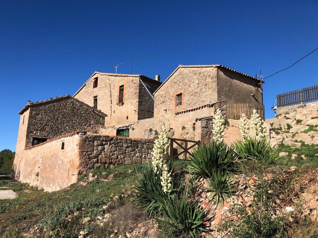 un antiguo edificio de piedra en una colina con flores blancas en Can Ollé, en Rubió
