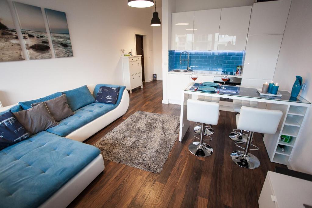 a living room with a blue couch and a kitchen at Apartament Nad Morzem in Darłówko