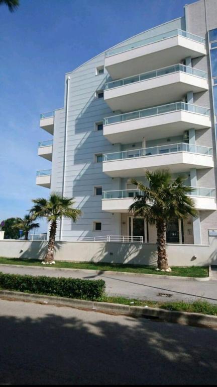 a white building with palm trees in front of it at Appartamento Azzurro in Roseto degli Abruzzi
