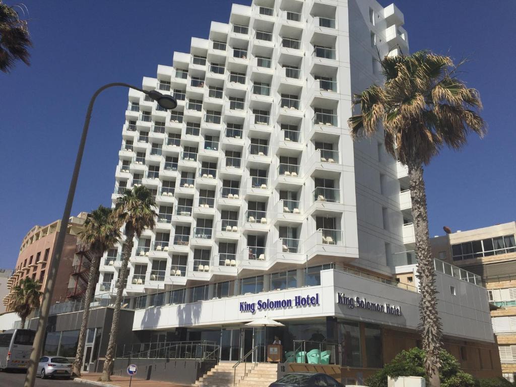 ein großes weißes Gebäude mit Palmen davor in der Unterkunft King Solomon Hotel in Netanya