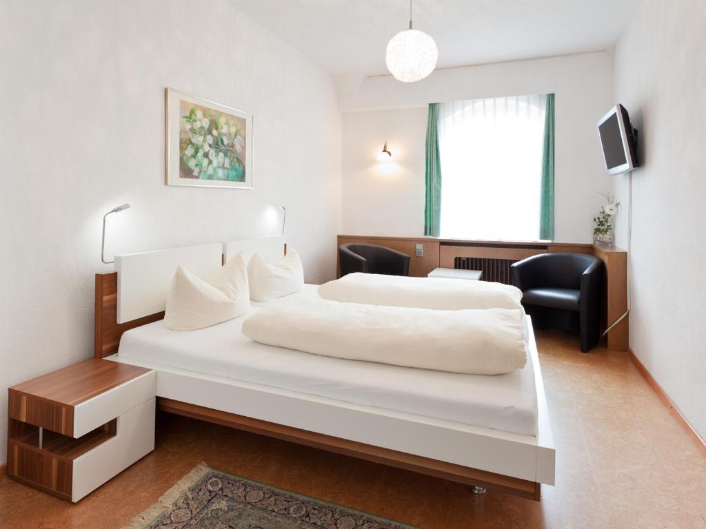 ein Hotelzimmer mit einem weißen Bett und einem Stuhl in der Unterkunft Hotel Kühler Krug in Freiburg im Breisgau