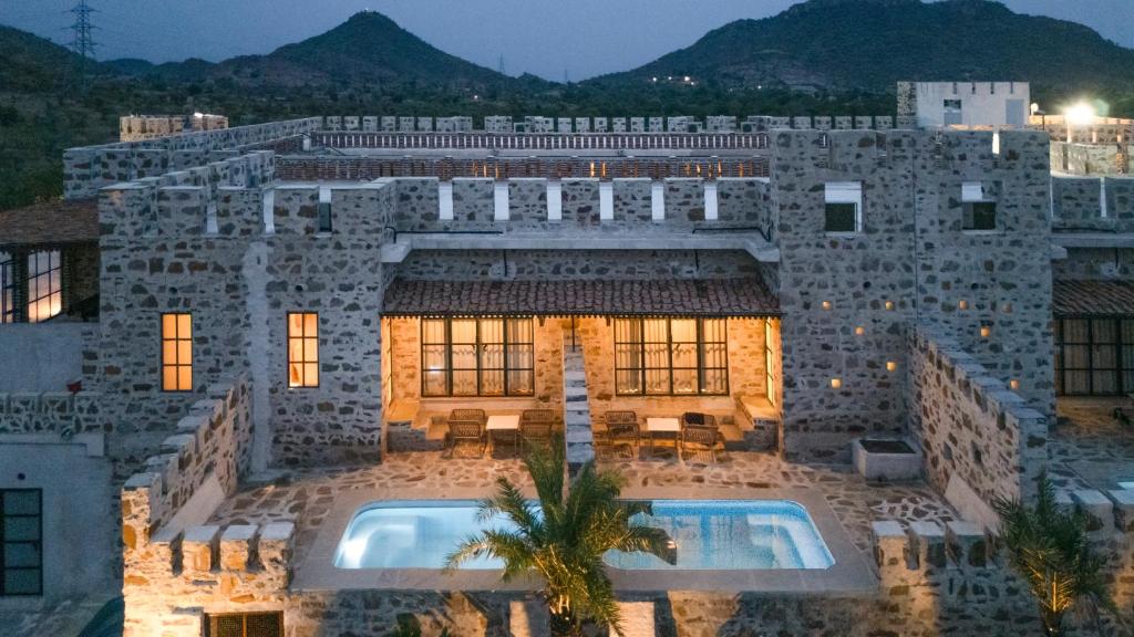 a large stone building with a swimming pool at Maya Luxury The Quila Udaipur in Udaipur