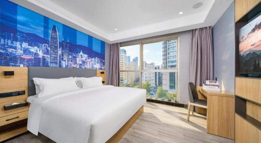 une chambre avec un lit blanc et un bureau et une grande fenêtre dans l'établissement Sheng Lin Na Hotel Minzhi Branch, à Shenzhen