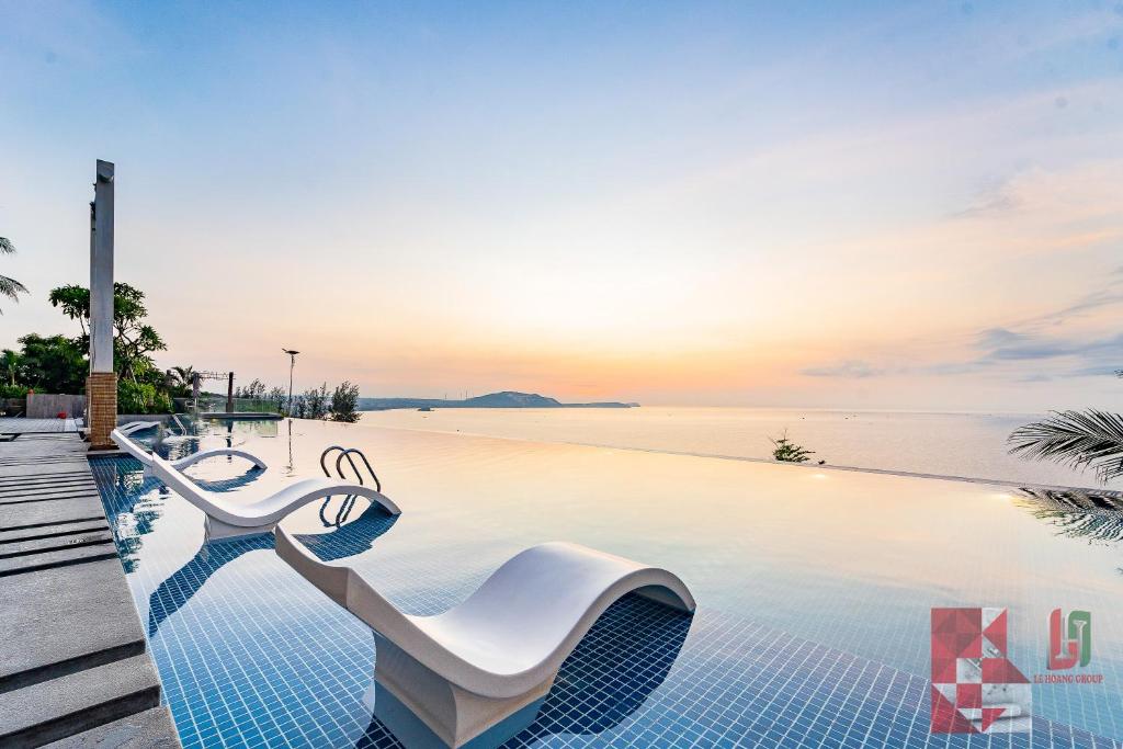 une piscine avec des chaises et l'océan en arrière-plan dans l'établissement Apec Mandala Mui Ne by LHG - Sea View, Infinity Pool, 17m to Bàu Trắng Bình Thuận, à Mui Ne