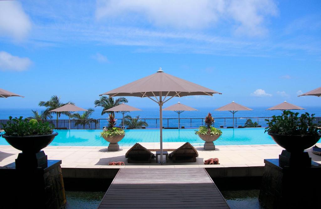 ein Resort mit einem Pool mit Sonnenschirmen und einem Tisch in der Unterkunft Sankara Hotel & Spa Yakushima in Yakushima