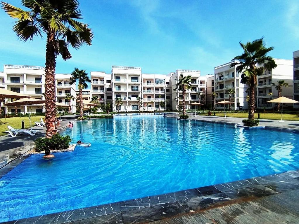 a large swimming pool with palm trees and buildings at Charming appartement in Bouznika in Bouznika