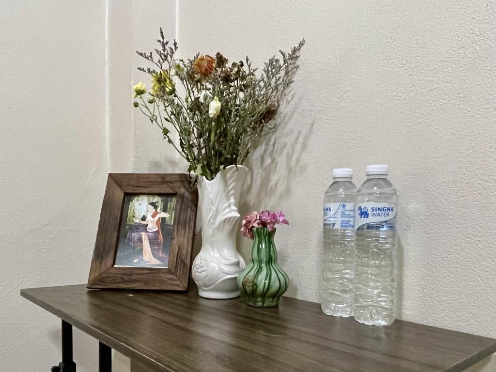 a table with a picture and a vase with flowers and water bottles at Yoga Bed and Breakfast in Chiang Mai