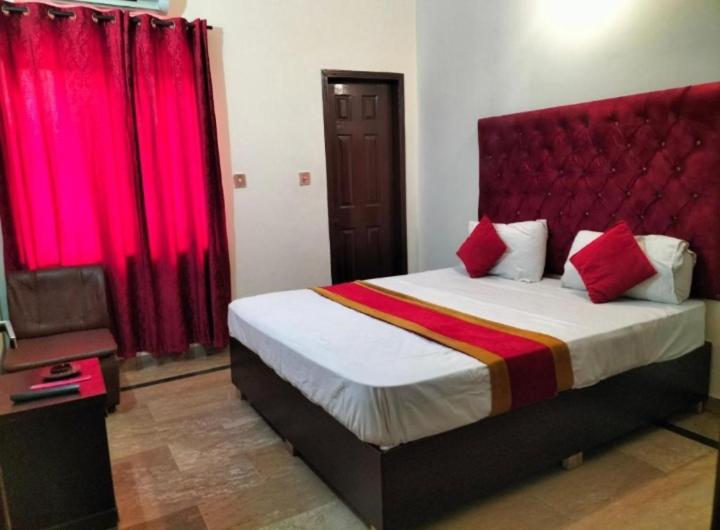 a bedroom with a large bed with red curtains at Second Home Family Hotel in Lahore